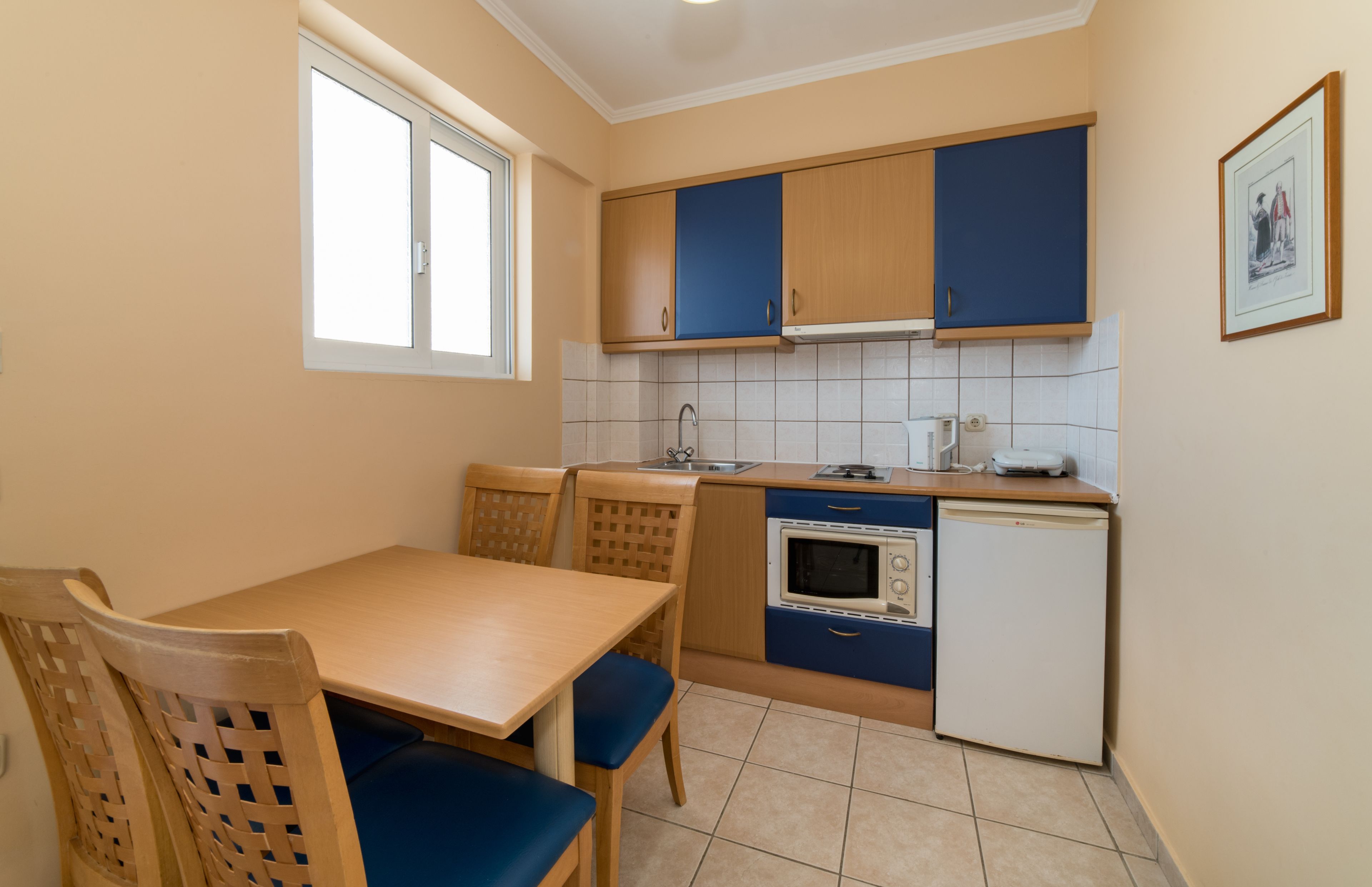 A compact kitchen with a dining table, chairs, a microwave, a refrigerator, and cabinets.