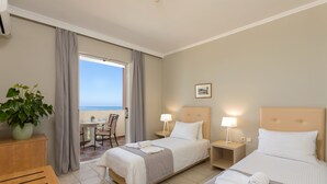 Habitación de hotel con dos camas, una mesita, una silla, una planta en maceta y vista al mar.