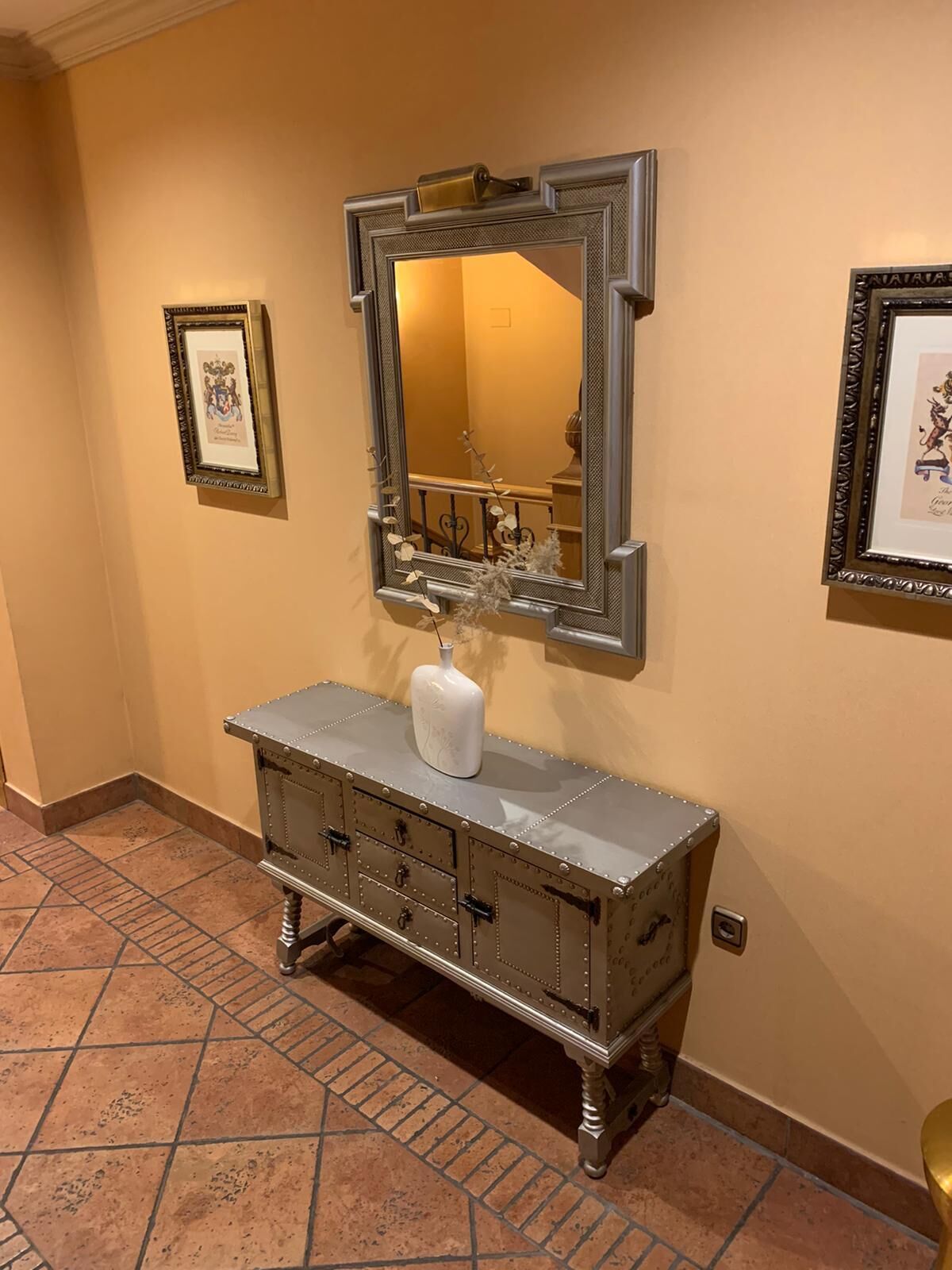 Un tocador de estilo vintage con un espejo grande, un jarrón blanco y un mueble metálico con cajones.