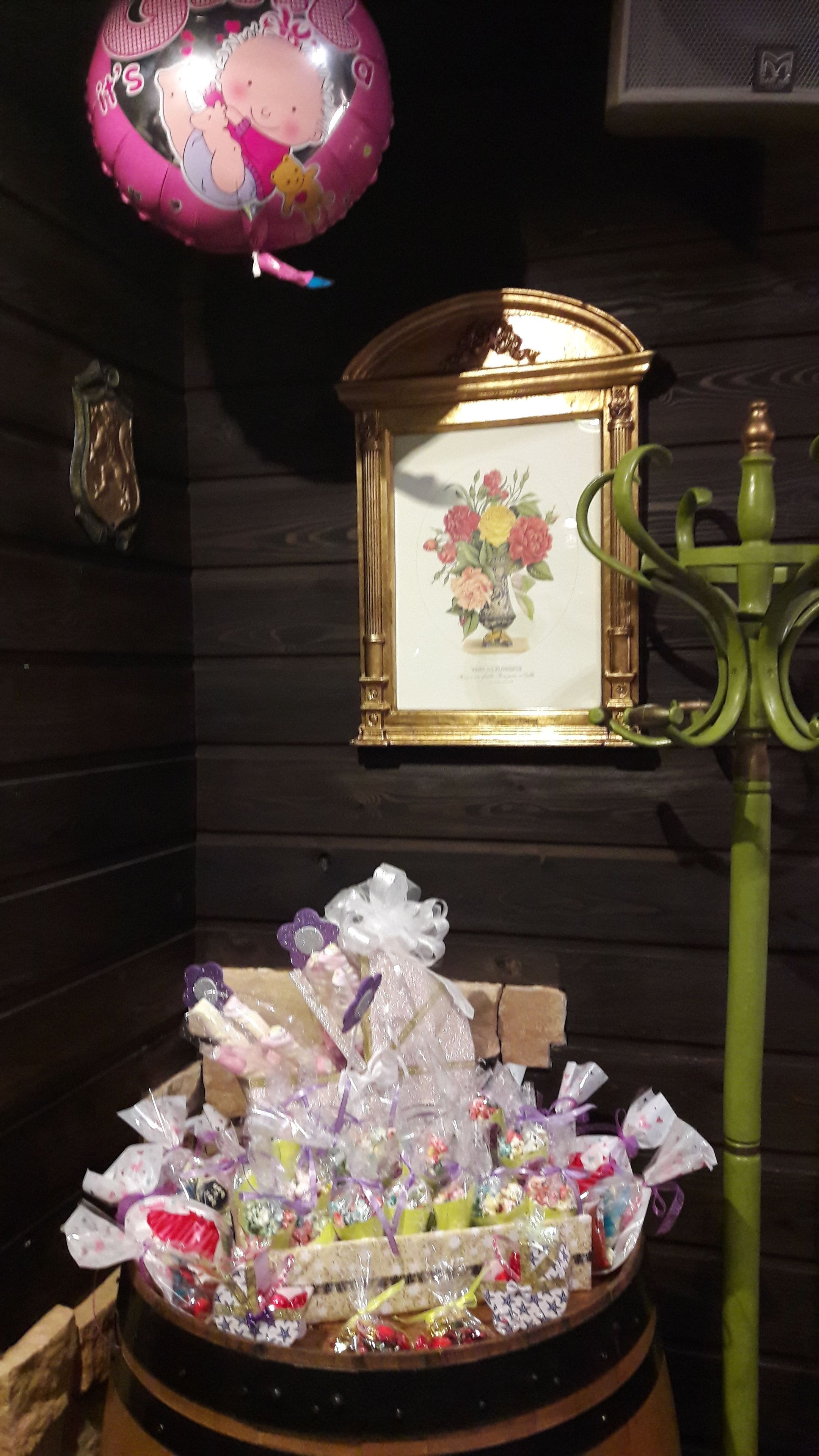 A room with a wooden wall, a framed picture of flowers, a green candelabra, and a table with wrapped gifts.