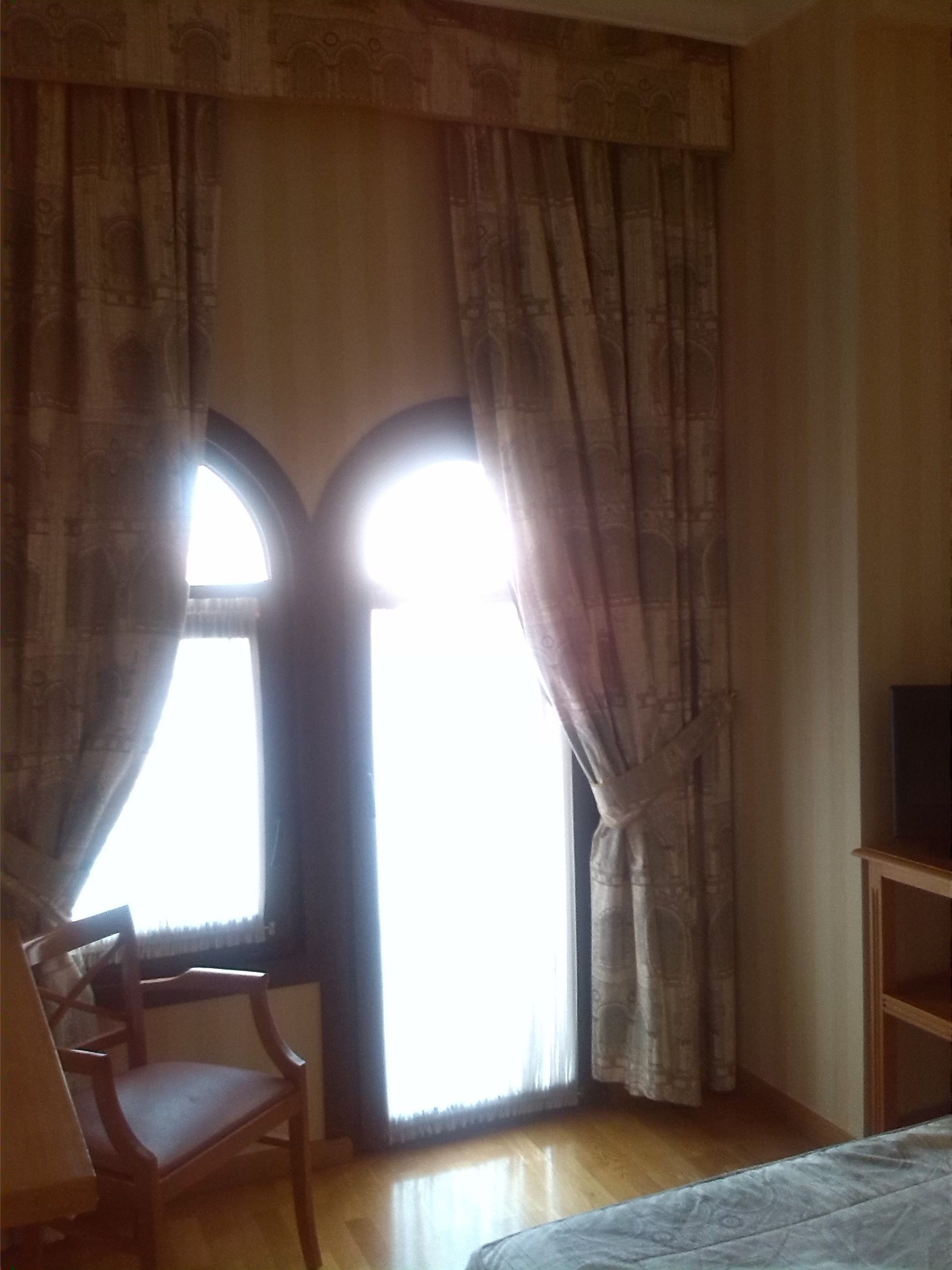 A room with a bed, a wooden chair, and a TV on a stand.