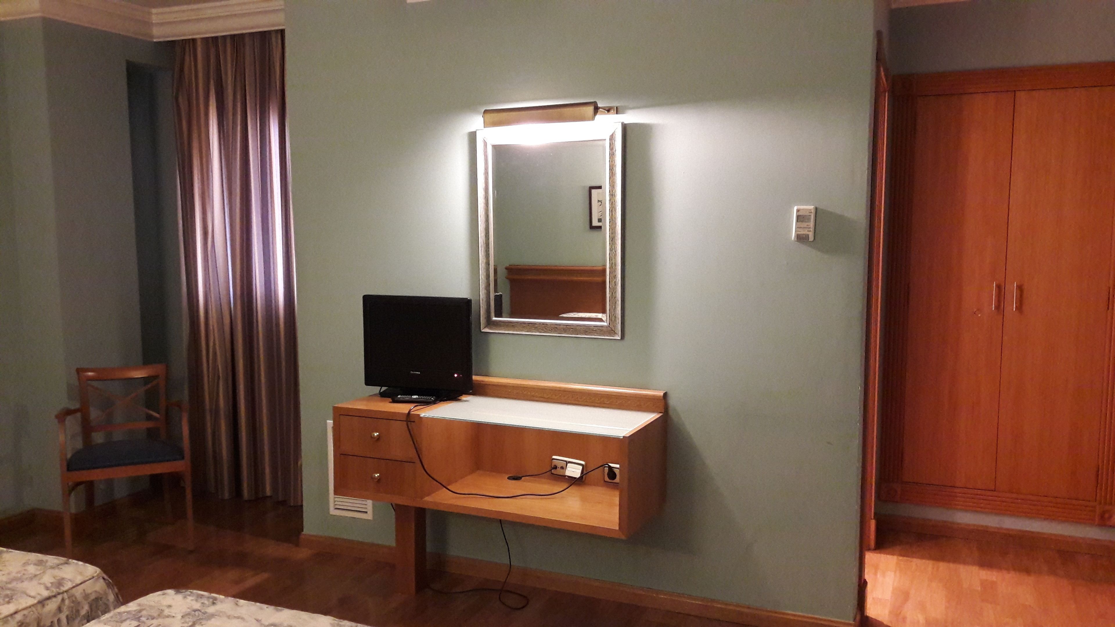 A hotel room with a wooden dresser, a television, a mirror, a wooden wardrobe, and a chair.