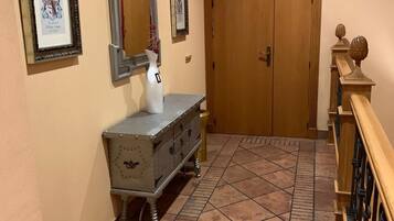 Un pasillo con piso de baldosas, una puerta de madera con la leyenda "3rd Plaza", un banco metálico y cuadros en la pared.