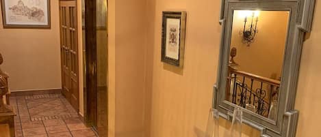 Un pasillo con suelo de baldosas, una consola de estilo vintage con objetos decorativos, un cuadro en la pared y una puerta que da a otra habitación.