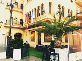 Un hotel con terraza al aire libre, palmeras y varias banderas.