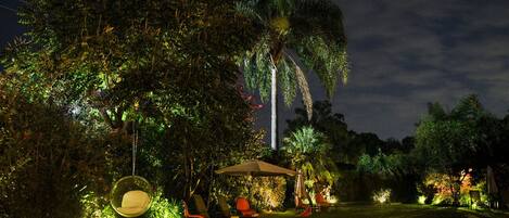 A garden with a swing chair, a covered seating area, and a palm tree.