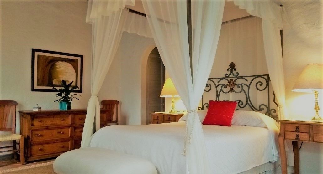 A bedroom with a four-poster bed, wooden dresser, and two bedside tables with lamps.