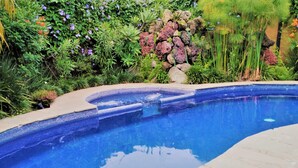 A swimming pool with a tiled edge, surrounded by lush greenery and various plants. - Areté (Tepoztlán)