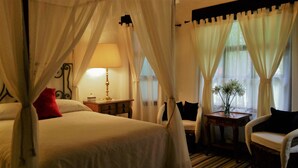 A hotel room with a bed, a nightstand, a lamp, a chair, and a window with curtains. - Areté (Tepoztlán)