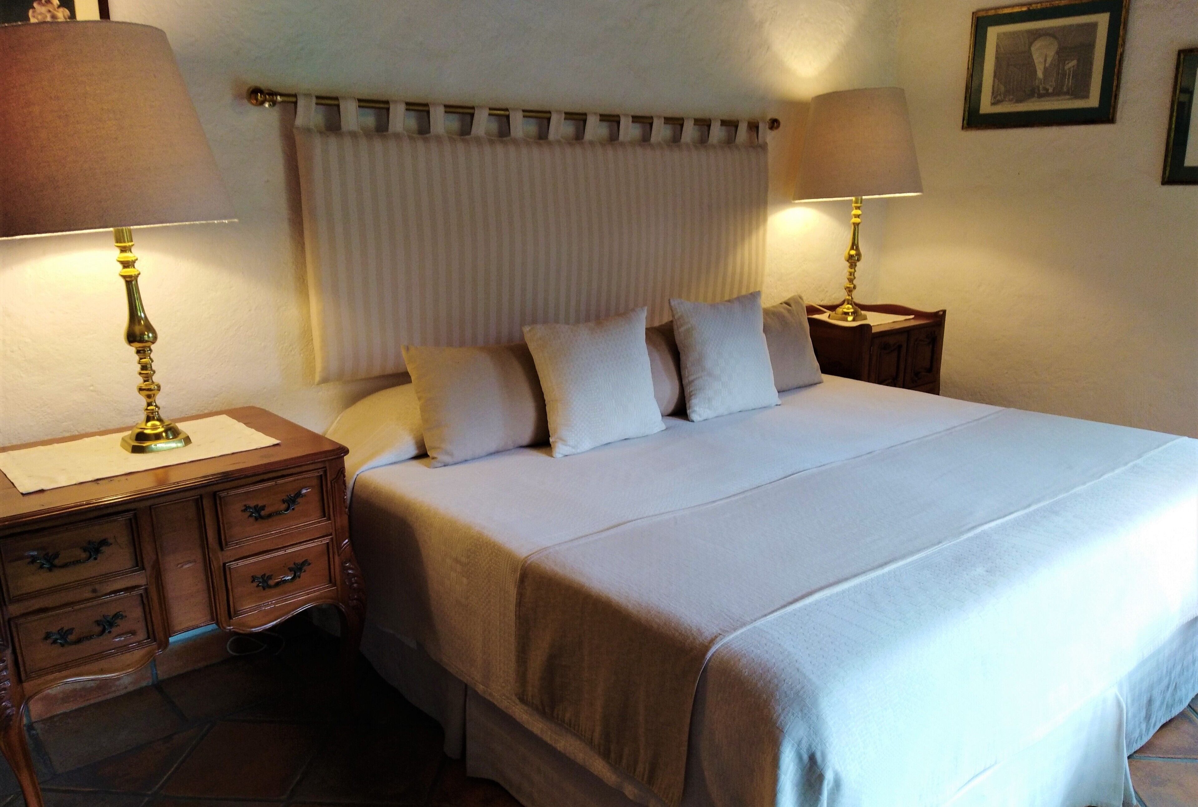 A neatly made bed with a white comforter and pillows, a wooden nightstand with a lamp, and a headboard with vertical slats.