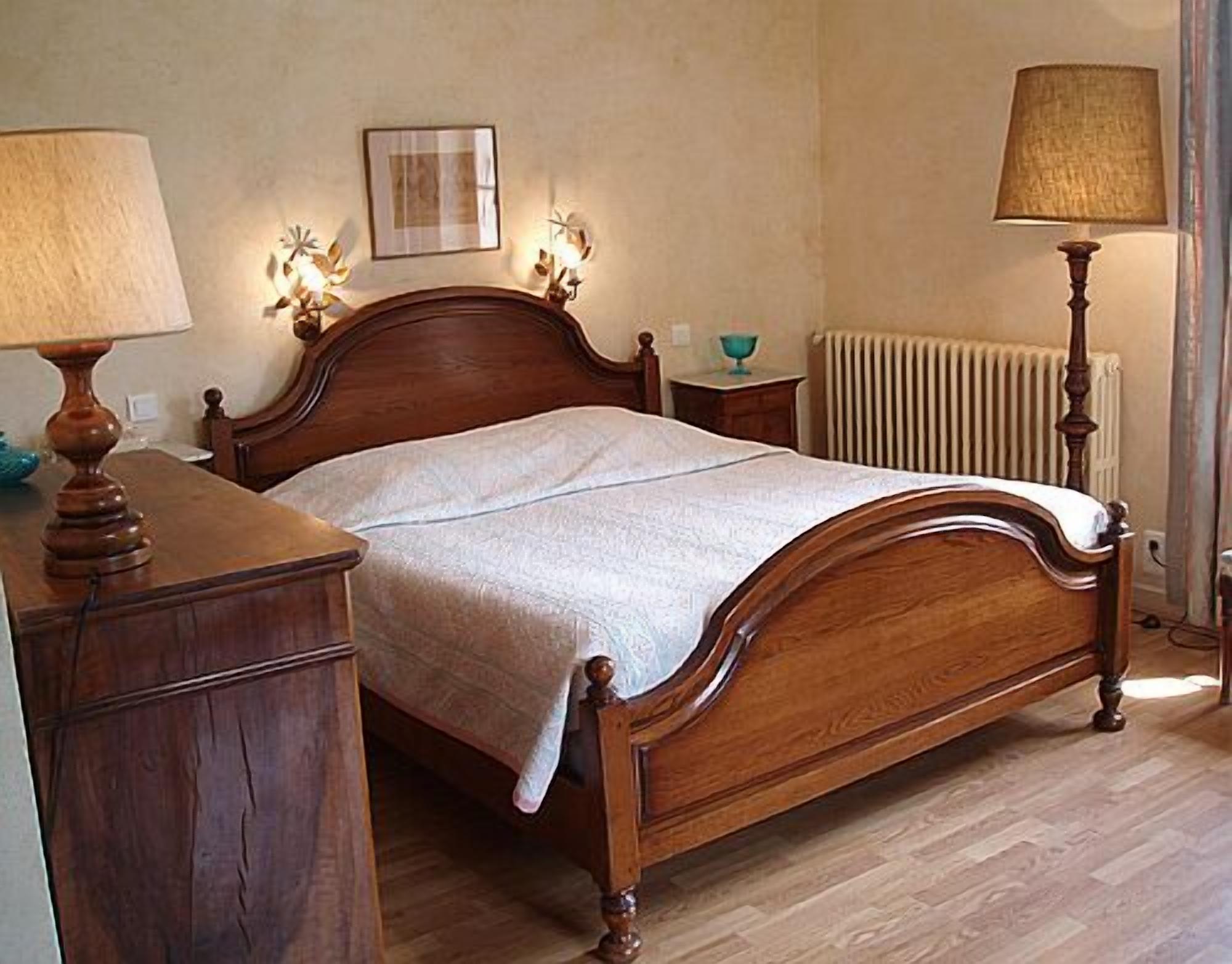 Una cama de madera con cabecero, una mesita de noche con lámpara, un cuadro colgado en la pared y un radiador.