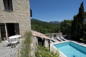 Un edificio de piedra con piscina, mobiliario exterior y vistas a las montañas.