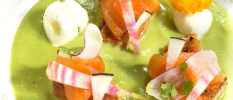 A white plate with a green sauce, salmon, radish slices, and a garnish.