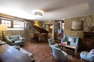 Una sala de estar acogedora con un piano de cola, dos sillones azul claro, una mesa de centro de madera y una pared de piedra.