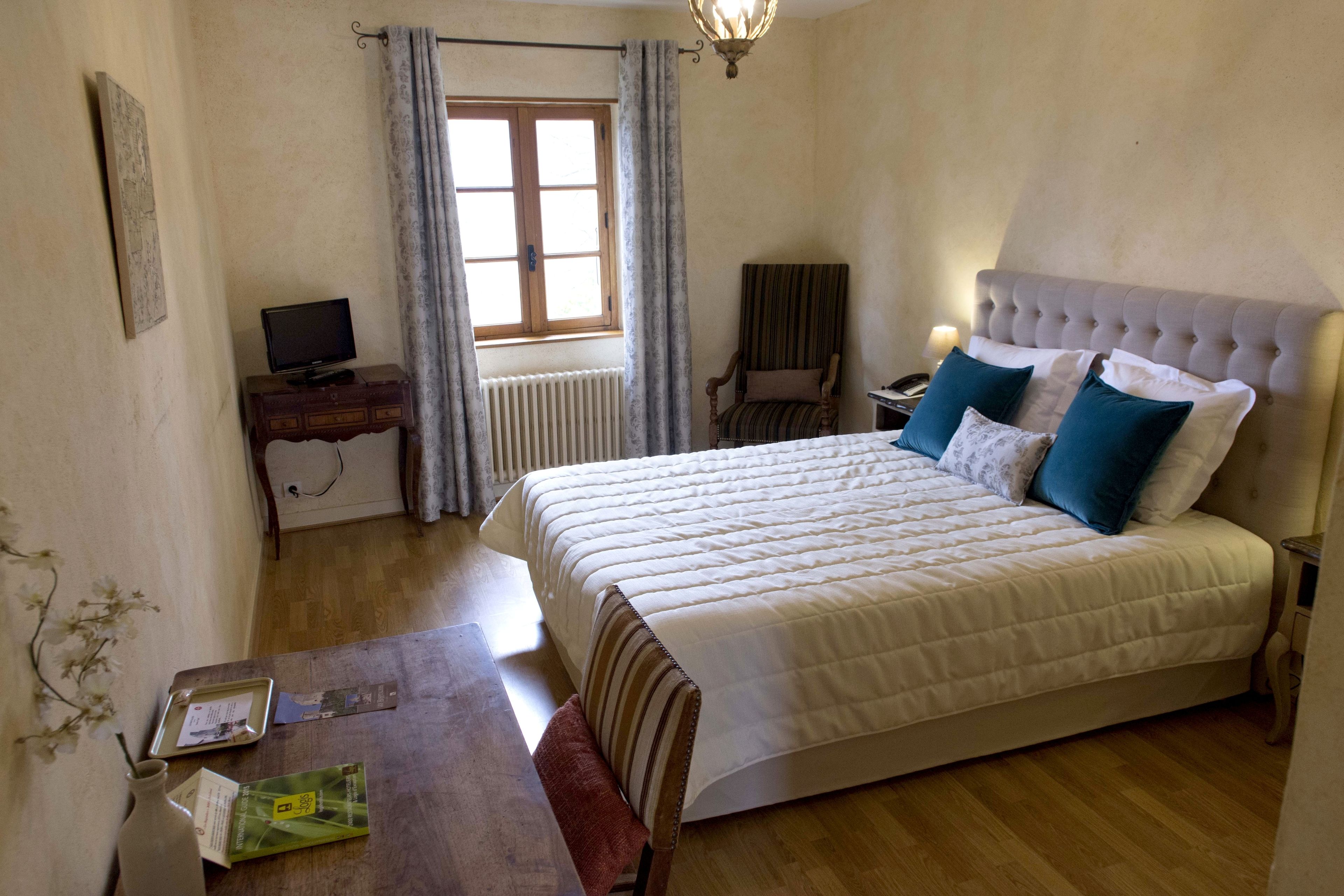 A bedroom with a bed, a desk, a chair, a television, and a window with curtains.