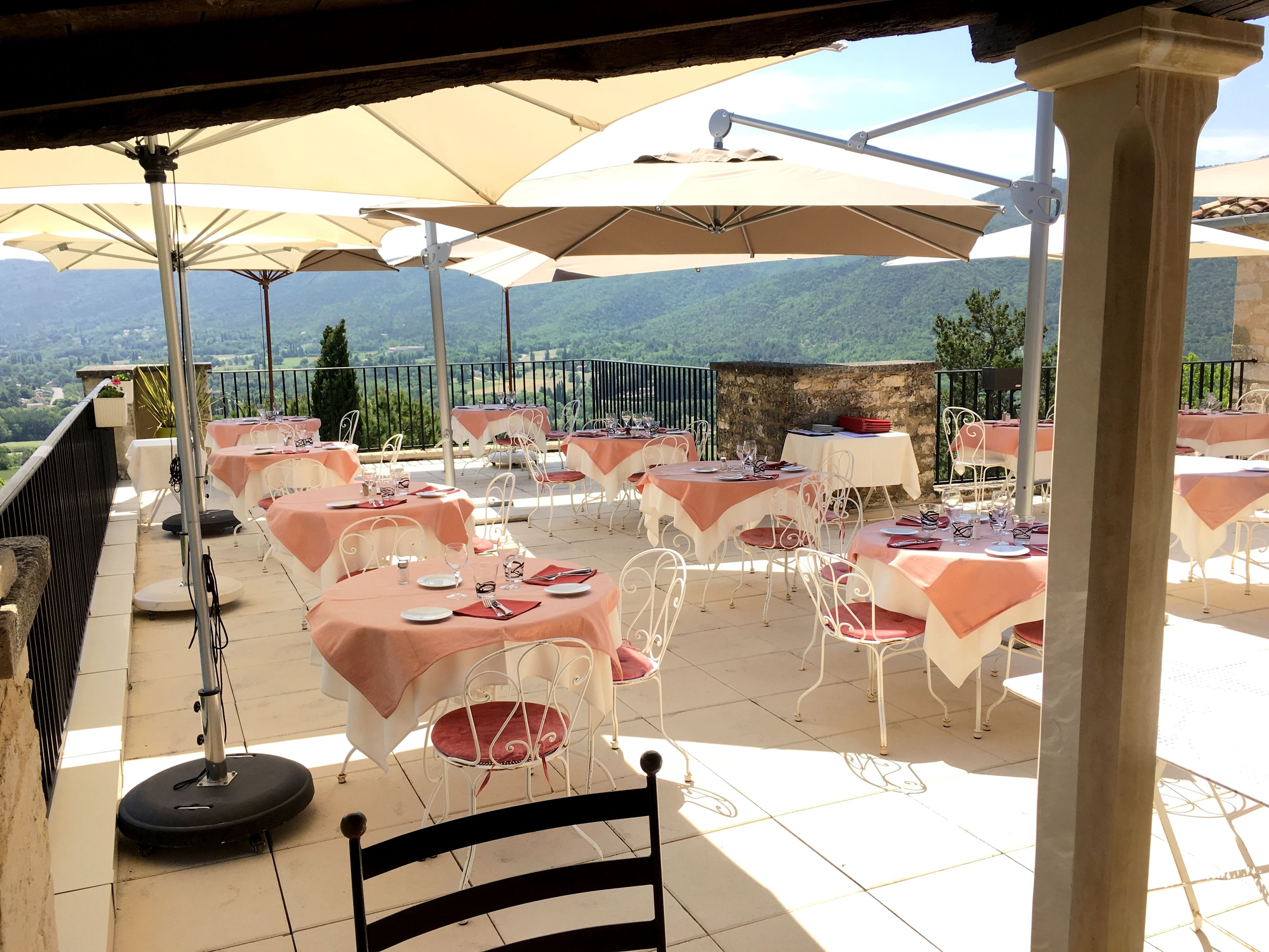 Un área de comedor al aire libre con mesas y sillas, protegida por sombrillas, con vistas a un paisaje pintoresco.