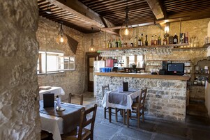 Una zona de bar rústica con paredes de piedra, vigas de madera y una variedad de botellas y copas en estantes.