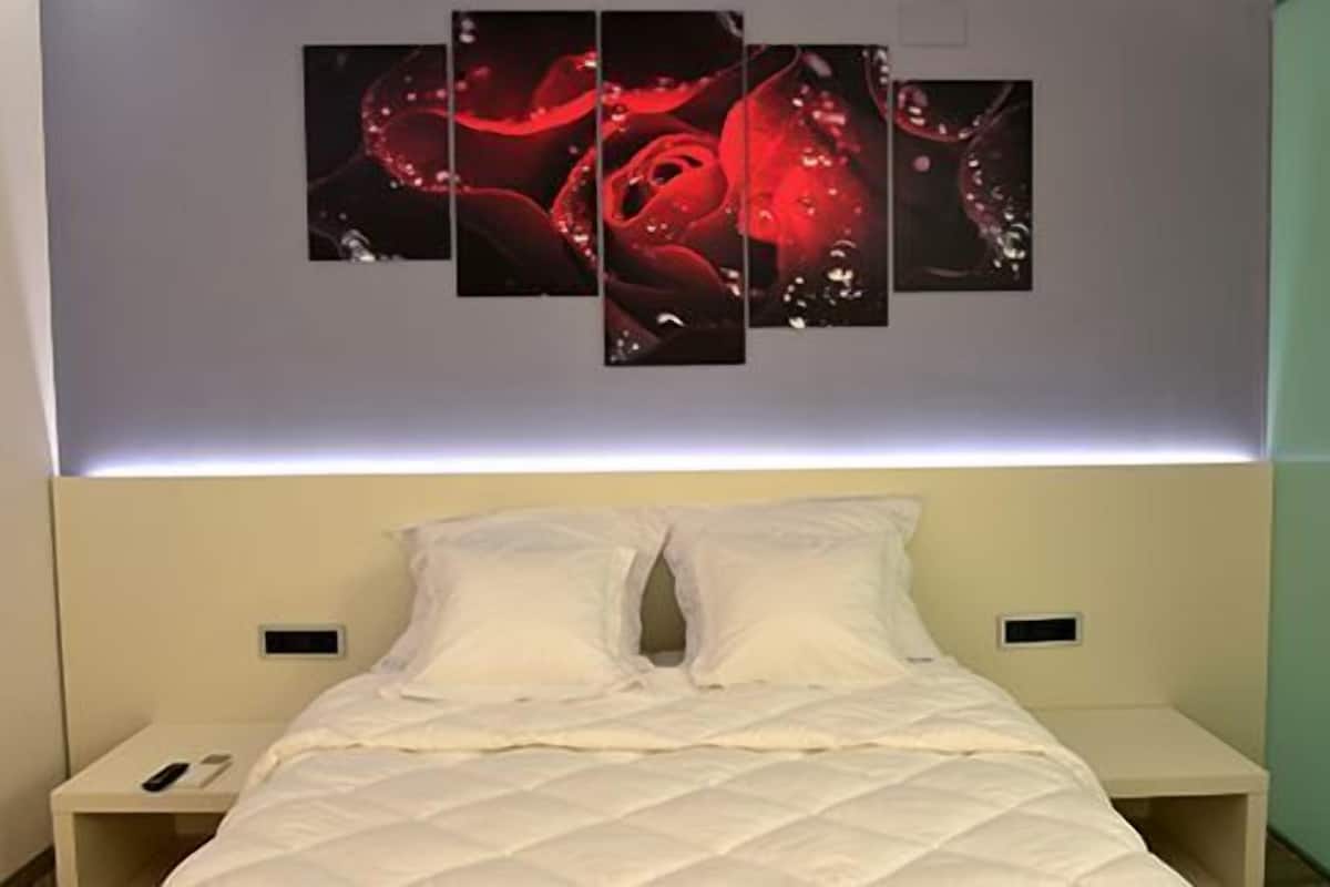 A hotel room with a bed, white bedding, and a wall-mounted artwork of red roses.