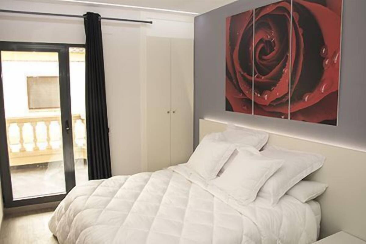 A bedroom with a bed, a door, and a large painting of a rose.