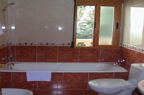 A bathroom with a bathtub, toilet, and a window with a view of greenery.