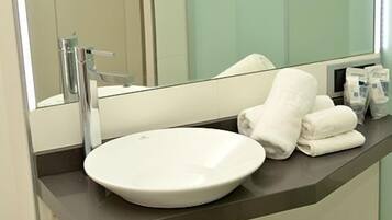 Un baño con un lavabo blanco, un espejo y toallas dobladas con cuidado sobre el mostrador.