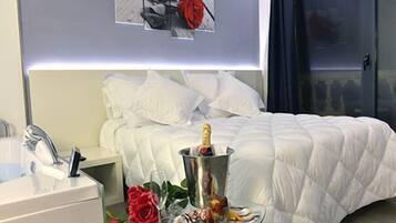 Habitación de hotel con cama, mesita de noche con una botella de champán, una copa y una rosa.