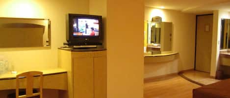 A hotel room with a TV on a stand, a desk, a chair, and a bed.