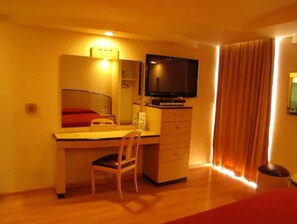 Una habitación de hotel con un escritorio de madera, una silla, un televisor y una cama.