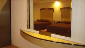 Habitación de hotel con un separador de vidrio curvo, una cama, una mesita de noche y un espejo que refleja la habitación.