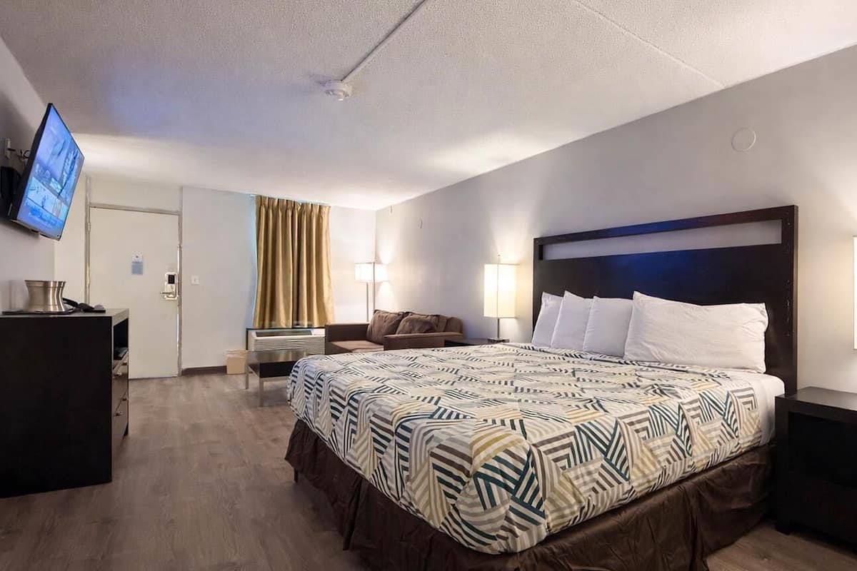 A hotel room with a large bed, two bedside lamps, a flat-screen TV, a desk, and a chair.