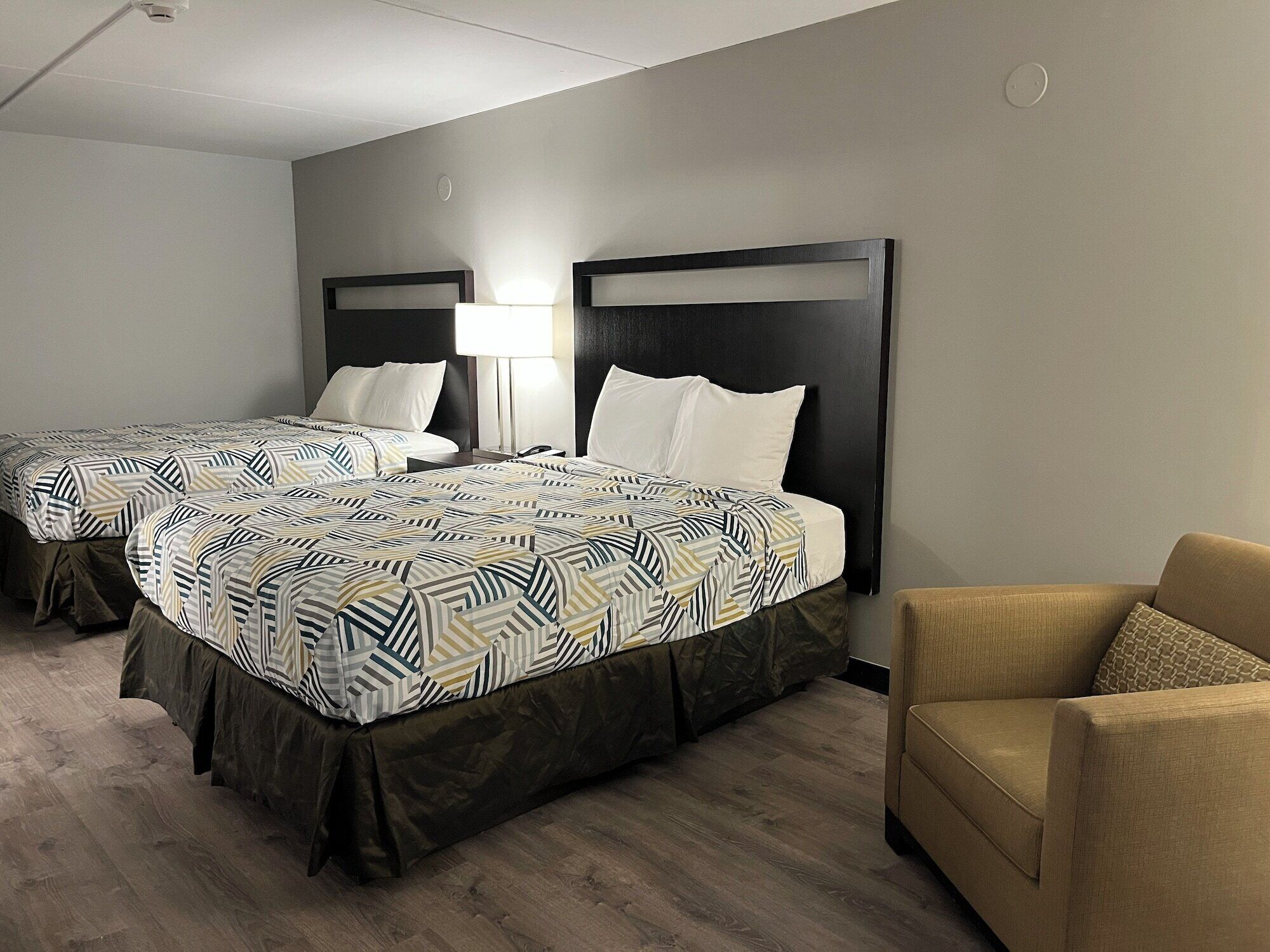 A hotel room with two beds, a sofa, and a lamp.