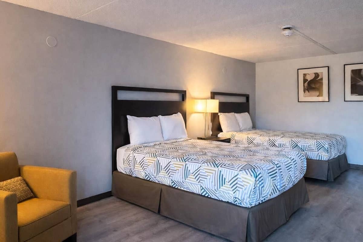 A hotel room with two beds, a sofa, and a wall-mounted lamp.