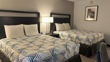 Habitación de hotel con dos camas, cada una con una colcha estampada y almohadas blancas. Entre las camas hay una mesita de noche con una lámpara, y un cuadro enmarcado en la pared.