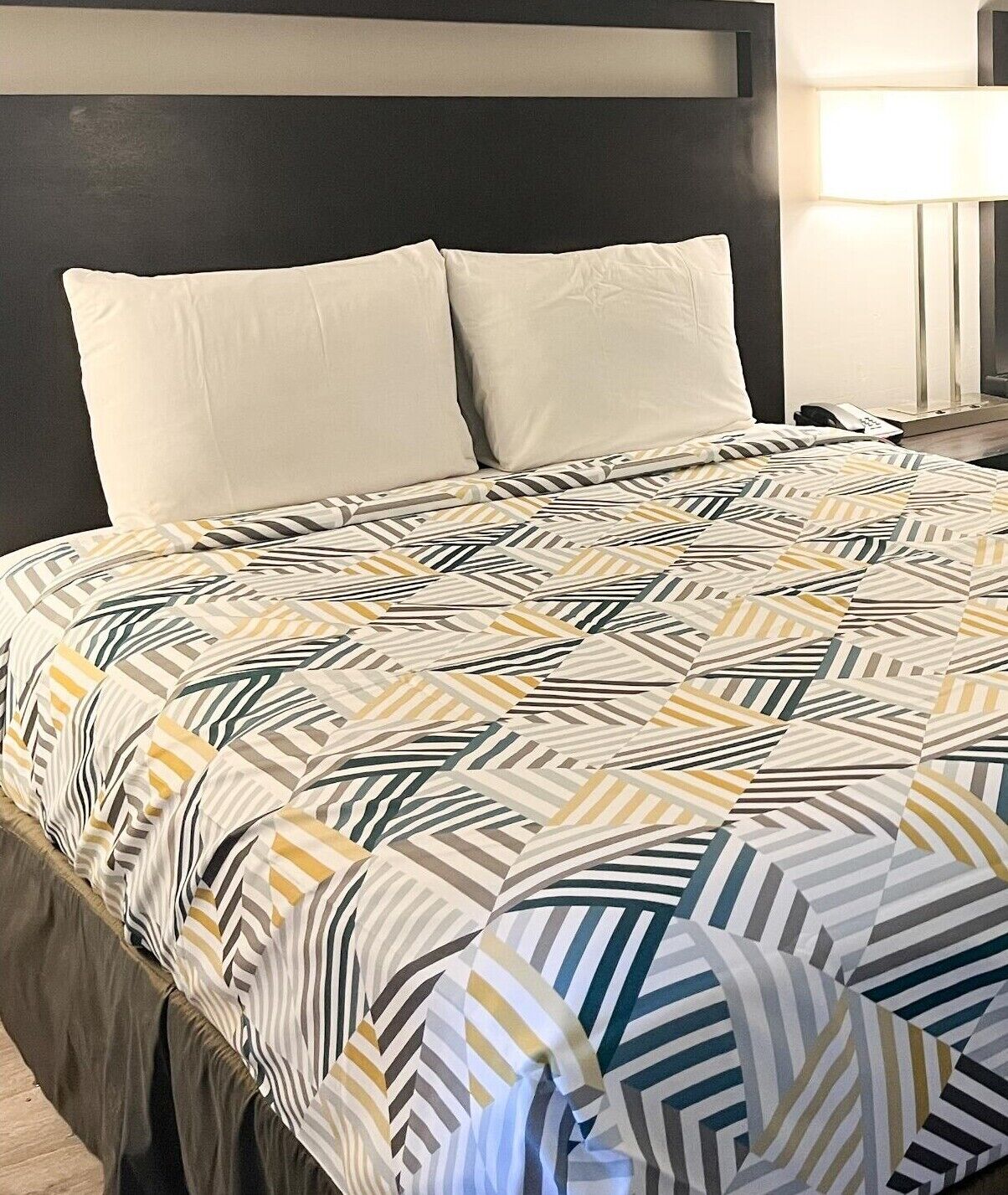 A neatly made bed with a patterned bedspread, two pillows, and a bedside table with a lamp.