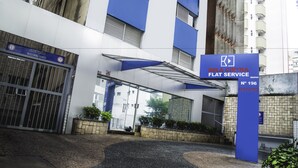 Entrada de un edificio con un letrero azul que dice 'BELA CINTRA FLAT SERVICE' y una puerta con la leyenda 'ATENÇÃO GARAGEI BAIXA'.