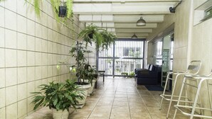 Un pasillo con paredes de baldosas, plantas colgantes, un sofá y taburetes metálicos.