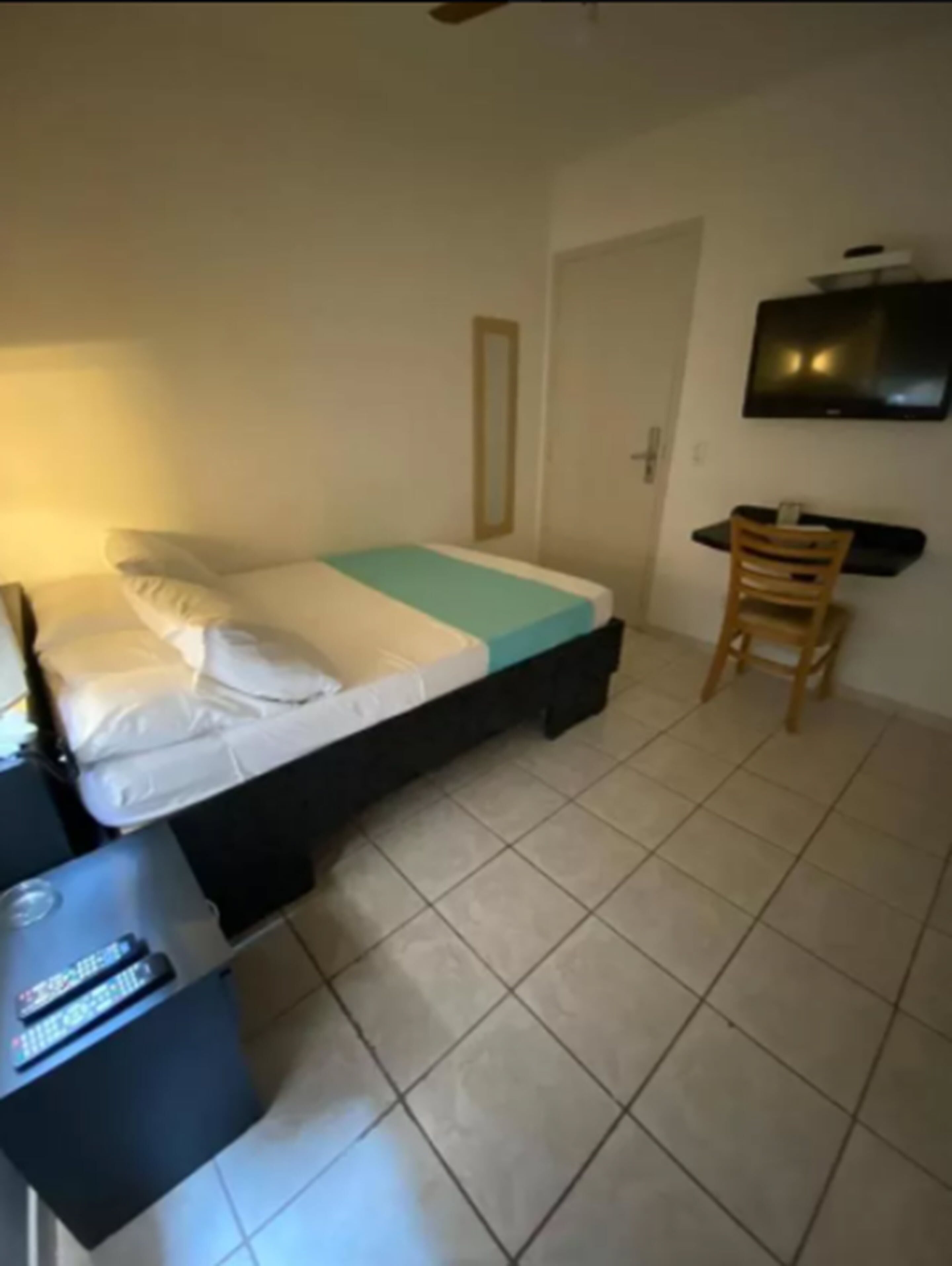 Una habitación pequeña y sencilla con cama, escritorio, silla y televisión.