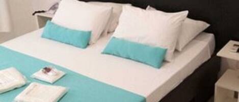 A neatly made bed with white and teal bedding, a black headboard, and a small bedside table with a lamp.