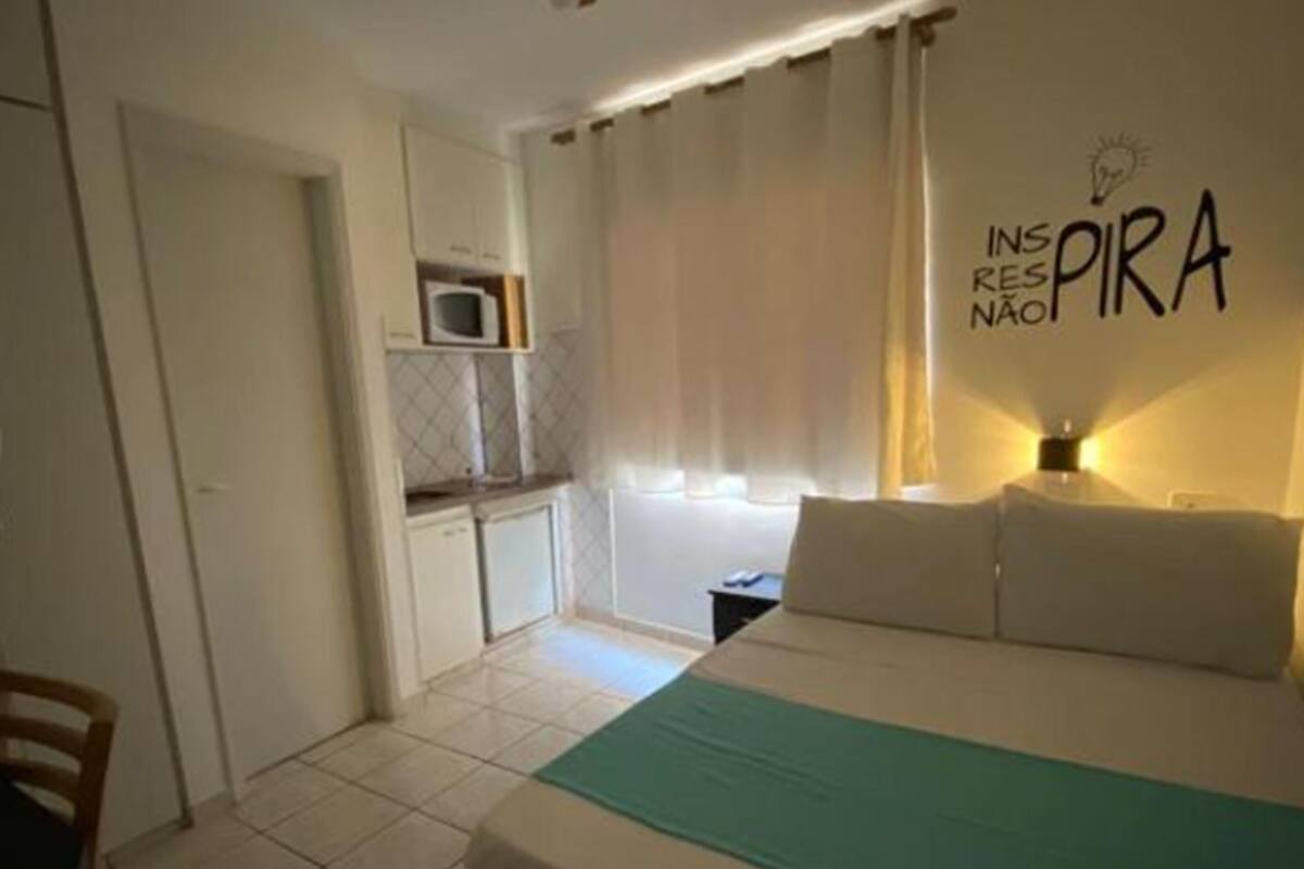 A bedroom with a bed, a ceiling fan, a kitchenette, and a wall with motivational text.