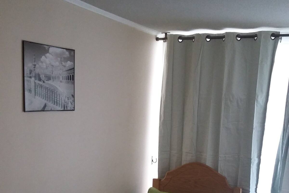 A bedroom with a bed, a picture on the wall, and a window with curtains.
