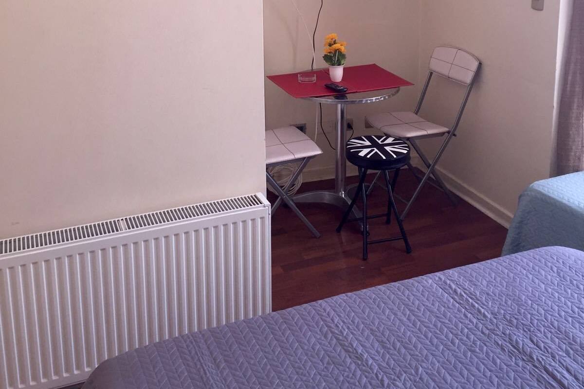 A small room with a bed, a TV mounted on the wall, a table with a chair, and a radiator.
