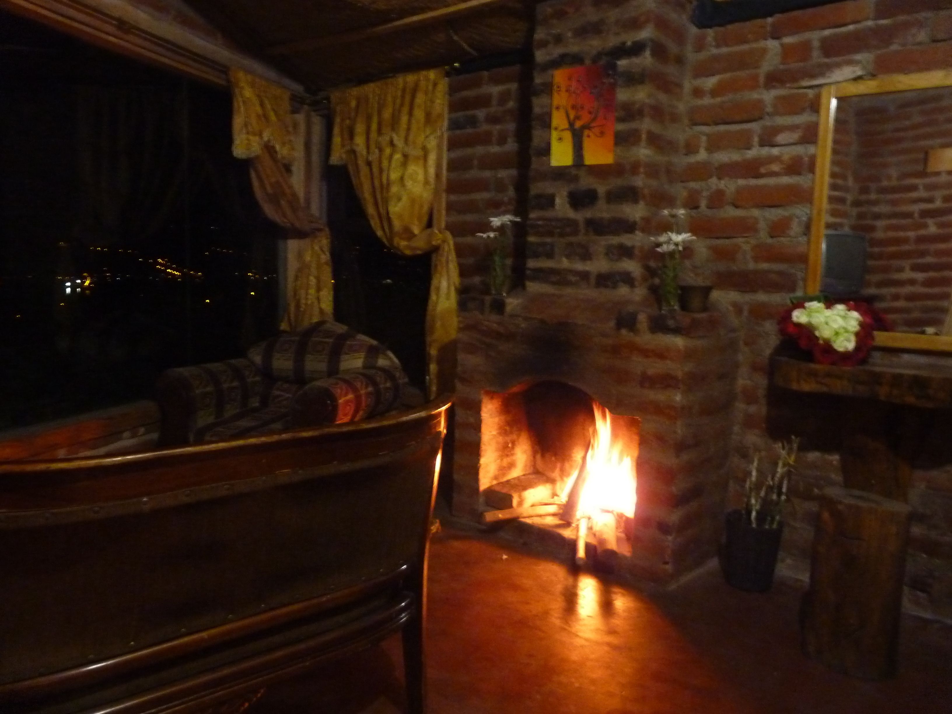 A cozy room with a brick fireplace, a sofa, and a window with curtains.