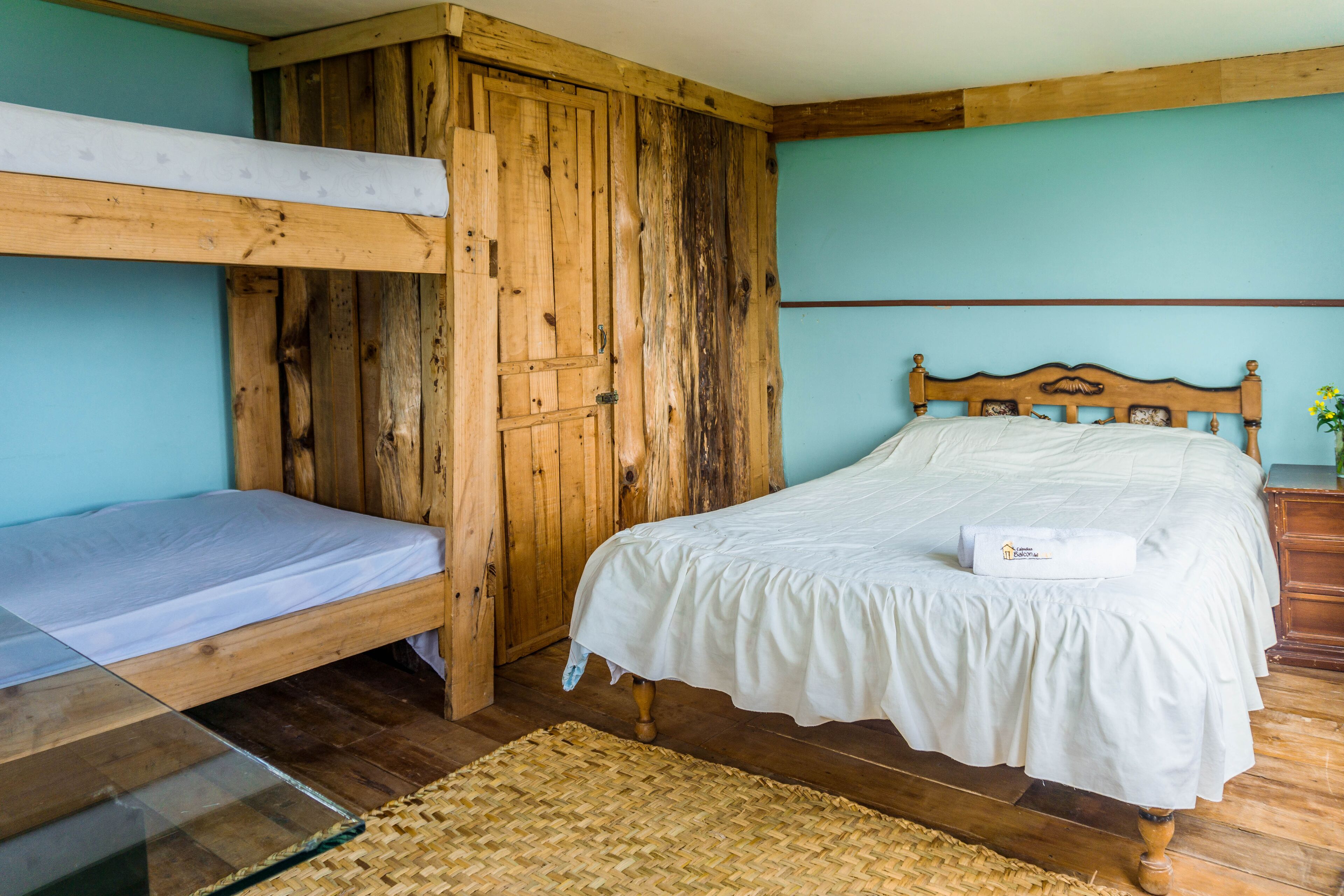 A room with a bunk bed, a single bed, wooden walls, and a woven rug.