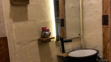 A rustic bathroom with a white toilet, a black basin, and a mirror.
