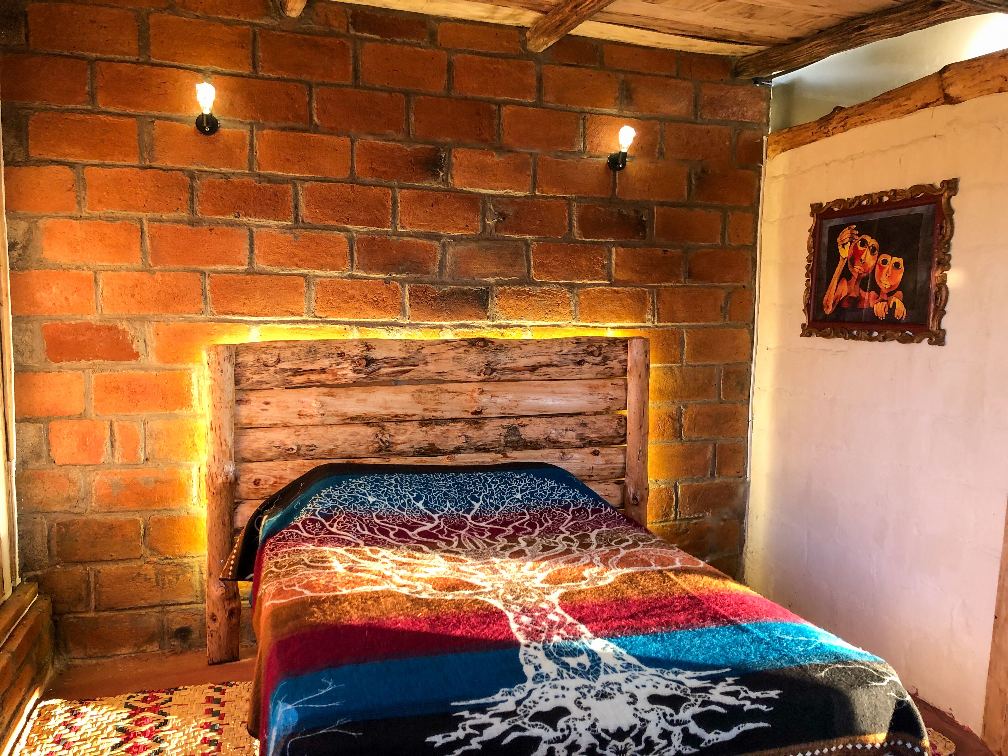 Una habitación con pared de ladrillo, cabecera de madera y manta colorida.