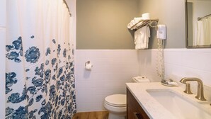 A bathroom with a shower curtain, toilet, sink, and towel rack. - Iron Masters - Inn on Main (Lakeville)