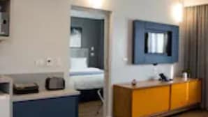 Een moderne hotelkamer met een bed, een bureau, een aan de muur bevestigde televisie en een klein zithoekje.