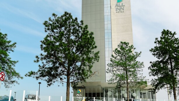 Een modern All Inn Hotel gebouw, omringd door bomen en parkeerauto's, met een opvallend logo.