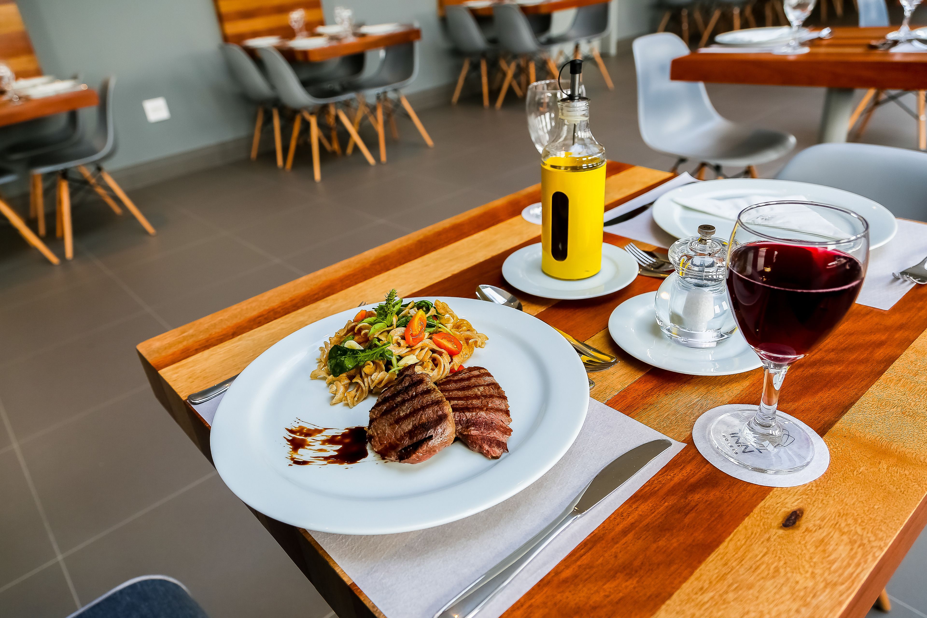 A dining table with a meal consisting of grilled meat, pasta, and a glass of red wine.