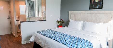 A hotel room with a large bed, a bedside table, a mirror, and a painting on the wall.